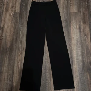 Svarta wide kostymbyxor Vero Moda - Svarta kostymbyxor från Vero Moda med klassisk design och breda ben. Byxorna har hällor för bälte och en rak, loose passform som ger en chill och stilren look. Perfekta att matcha med sneakers eller boots för en trendig vibe.