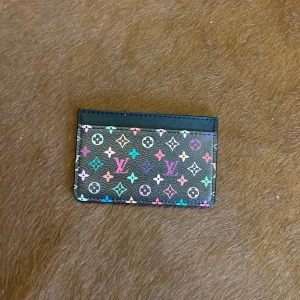 Louis Vuitton plånbok med färgglatt mönster - Snygg plånbok från Louis Vuitton med klassiskt monogram i flera färger på svart bakgrund. Slimmad design med plats för kort, perfekt att ha i fickan. Materialet är skinn och mönstret är riktigt färgstarkt och sticker ut.