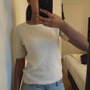 Vit stickad kortärmad tröja - Säljer en enkel och stilren vit stickad tröja med korta ärmar och rund hals. Tröjan har en mjuk känsla och ribbad kant vid halsen och nederkanten. Perfekt att matcha med jeans eller kjol för en clean look.