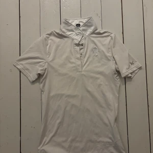 Vit henley från Kingsland - Vit henley från Kingsland med korta ärmar och klassisk krage. Skjortan har knappar framtill och broderad logga på bröstet samt ett X på ena ärmen. Perfekt för dig som gillar stilren och sportig look.