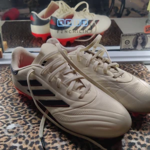 Adidas Copa fotbollsskor strl 38 - Säljer ett par Adidas Copa fotbollsskor i storlek 38. Skorna är vita med svarta och röda detaljer, har snörning och rund tå. Yttermaterialet är syntet och sulan är röd med dobbar för gräsplan. Perfekt för dig som vill ha stil på planen. Dom är nya och bara andvända ett fåtal gånger.