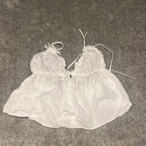 Vit linnetopp med snörning - Säljer en vit omlott linnetopp med snörning och knyt i axelbanden. Toppen har en luftig och voluminös passform med rynkade detaljer och öppen rygg. Perfekt för varma dagar och sommarhäng. Materialet känns lätt och svalt mot huden.