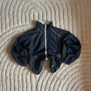 Mörkblå vindjacka från Superpros - Snygg mörkblå vindjacka från Superpros i storlek S. Jackan har vita detaljer längs dragkedjan och sömmarna, samt meshfoder på insidan. Hög krage och elastiska ärmslut ger en sportig vibe. Perfekt för dig som gillar stilren och funktionell design.