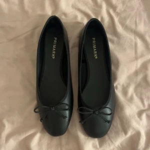 Svarta ballerinaskor från Primark - Stilrena svarta ballerinaskor från Primark med rund tå och en söt rosettdetalj framtill. Skorna har en platt sula och är tillverkade i syntetmaterial som ger en klassisk look. Perfekta att matcha med jeans eller klänning för en enkel och snygg stil. Har aldrig haft på mig dom 