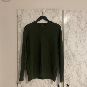 Mörkgrön stickad tröja  - En stilren mörkgrön stickad tröja från Weekday med rund halsringning och långa ärmar. Tröjan har en enkel och clean design som passar perfekt till jeans eller chinos. Materialet är mjukt och skönt, perfekt för kyligare dagar.