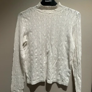 Vit stickad tröja från KappAhl - Vit stickad tröja från KappAhl med diskret mönster och hög hals. Tröjan har lång ärm och en klassisk passform.