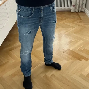 Replay Anbass slitna jeans, blå - Säljer ett par Replay Anbass jeans i blå tvätt med slitningar och hål på benen. Modellen är slim fit med klassisk femficksdesign och normal midja. Jeansen har snygga slitdetaljer och är tillverkade i mjukt denimtyg. Längd 32 och Midja 29