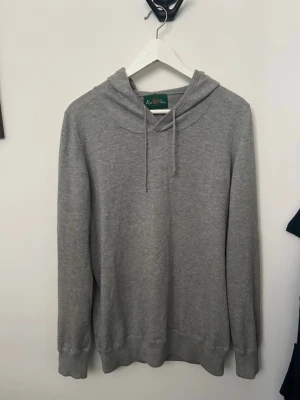 Grå basic hoodie med huva - Enkel och stilren grå hoodie med huva och dragsnören. Tillverkad i mjukt material och har långa ärmar samt ribbade muddar vid ärmslut och nederkant. Perfekt för en avslappnad look och passar till det mesta.