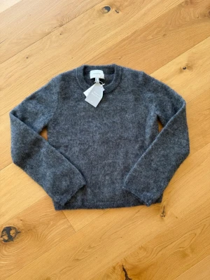 Mohairtröja H&M Edition - Mysig stickad tröja i grå mohair- och ullblandning från H&M Edition. Tröjan har rund halsringning, långa ärmar och en fluffig, mjuk känsla. Perfekt för kyliga dagar och enkel att matcha med olika outfits. Helt oanvänd med lappen kvar. Strl S.