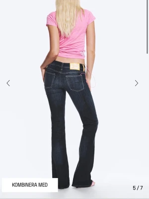 Mörkblå bootcut jeans med kontrastsömmar - Snygga mörkblå bootcut jeans med vita kontrastsömmar och klassiska bakfickor. Jeansen har låg midja och en gul patch bak i linningen. Perfekta för en trendig och avslappnad stil.