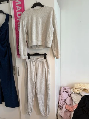 Grått loungewear-set i mjuk bomull - Säljer ett grått loungewear-set med sweatshirt och matchande byxor. Tröjan har rund hals och långa ärmar, byxorna har resår i midjan och vid benslut. Perfekt för chill dagar hemma eller när du vill vara bekväm. Materialet känns mjukt och skönt mot huden.