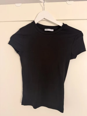 Svart basic t-shirt från Bershka - En svart, enkel och tight t-shirt från Bershka. Klassisk rund halsringning och korta ärmar. Perfekt att matcha med jeans eller kjol för en clean look. Tillverkad i mjuk bomull som känns skön mot huden.