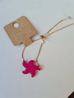 Guldhalsband med rosa sjöstjärna - Unikt halsband med en tunn guldfärgad kedja och en rosa sjöstjärna som hänge. Kedjan har justerbar längd med små guldfärgade kulor i ändarna. Hänget är gjort för hand av mig i polymerlera. 