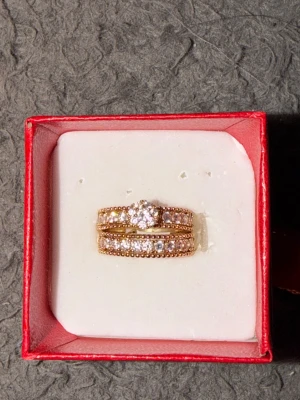 Guldfärgad ring med gnistrande stenar - Säljer en guldfärgad ring med flera gnistrande stenar och pärldetaljer runt om. Ringen har en elegant design med en större sten i mitten och mindre stenar längs bandet. Perfekt för dig som gillar bling och vill sticka ut.