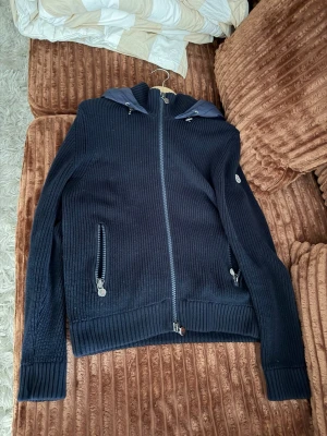 Mörkblå jacka Moncler  - Snygg mörkblå stickad jacka från Moncler med dragkedja framtill och två fickor med dragkedja. Tröjan har ribbade muddar och en huva med dragsko. Perfekt för dig som gillar exklusiva och stilrena plagg. Funkar sena sommar kvällar och höst,vår ( hör av er vid frågor, kan såklart gå ner i pris lite vid snabb affär)