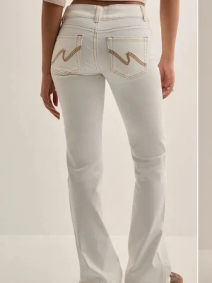 Vita bootcut jeans  - Säljer ett par vita bootcut jeans med snygga kontrastsömmar och ikoniska zigzag-detaljer på bakfickorna. Jeansen har hög midja och klassisk femficksdesign. Perfekta för dig som vill ha en clean men ändå unik look. Nypris: 699 kr