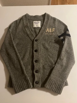Abercrombie & Fitch cardigan (väldigt sällsynt) - Abercrombie & fitch stickad cardigan i grå färg. Riktigt snygg och sällsynt säljs inte längre. Storlek S/M passar 168-178 cm lång i perfekt skick som ny. Pris 628 kr ej hugget i sten!