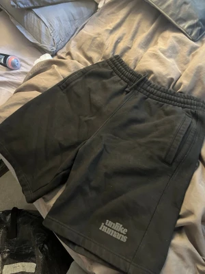 Svarta shorts från Unlike Humans - Svarta shorts från Unlike Humans med elastisk midja och två sidofickor. Tillverkade i mjukt material som känns skönt mot huden. Perfekta för chill dagar eller när du vill ha en avslappnad stil.