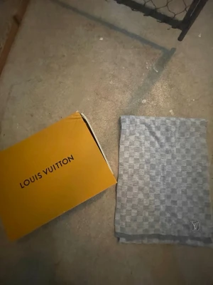 Grå halsduk m mönster  - Snygg grå halsduk med klassiskt rutmönster och logga i hörnet. Halsduken är rektangulär och har en stilren design som passar till det mesta. Perfekt accessoar för dig som gillar exklusiva detaljer.