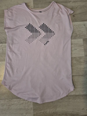 Ljusrosa t-shirt från 157 Funk - Ljusrosa t-shirt från 157 Funk med svart grafiskt tryck framtill. T-shirten har rund halsringning och är kortärmad med en något längre, rundad nederkant. Tillverkad i mjuk bomull som känns skön mot huden.