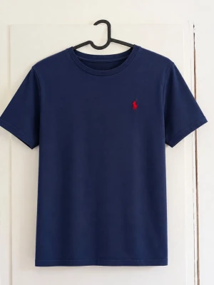 Polo Ralph Lauren marinblå T-shirt – M / 10–12 år - Klassisk marinblå T-shirt från Polo Ralph Lauren med röd broderad logga på bröstet 🐎 Rund hals och stilren modell som är lätt att matcha med jeans, shorts eller chinos. Storlek: M (10–12 år) / 150 cm Färg: Marinblå med röd logga Skick: Fint begagnat skick utan defekter förutom att den är lite färg blekt! Tillverkad i Indien. Hör gärna av dig vid frågor eller om du vill ha fler bilder 😊