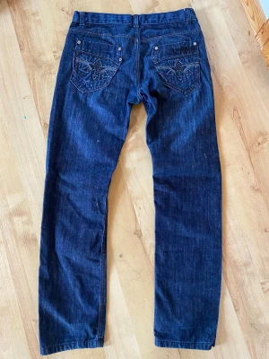 Y2K jeans - Mörkblåa y2k stil jeans med dekorationer som bl.a. stjärnor på bakfickorna, knapp saknas. Rak passform. Passar ungefär som storlek 36
