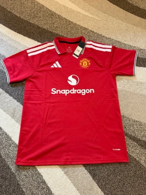 Manchester United 26-27 hemmatröja - Manchester United 26-27 hemmatröja  Storlek: XL Namn och nummer: ingen Badge: ingen  Beskrivning: Tröjan är helt ny och felfri.  Säljs av ICEKIT icekit.se