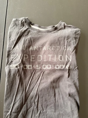 Sail Racing Antarctica Edition tröja 🖤 | 160 - Cool svart t-shirt från Sail Racing med trycket 'Sail Antarctica Expedition' och koordinater på bröstet. Klassisk rund hals och korta ärmar. Tillverkad i mjuk bomull som känns skön mot huden. Perfekt för dig som gillar äventyr och stilren design.