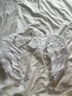 Vita ängelvingar  - Säljer ett par vita änglavingar med fjädrar, perfekta till maskerad eller halloween. Vingarna har elastiska band för enkel användning och är täckta med mjuka, vita fjädrar som ger en autentisk look. Passar till änglakostym eller temafest. Använd en gång 