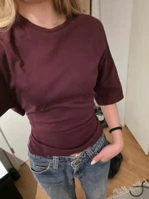 Vinröd topp med knyt i ryggen - Säljer en vinröd topp med halvlånga ärmar och snygg knytning i ryggen från Nelly!