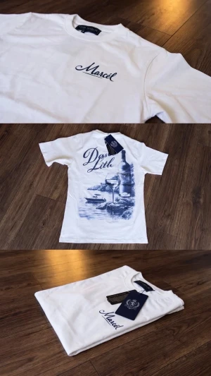 Vit t-shirt från Marcel med tryck - Vit t-shirt från Marcel med marinblå text på bröstet och stort grafiskt tryck på ryggen med motiv av vinflaska, glas och landskap. Klassisk passform och rund halsringning. Perfekt för dig som gillar stilrena plagg med unika detaljer.