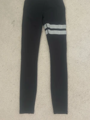 Svarta träningsbyxor  - Snygga svarta träningsbyxor med två vita mesh-ränder runt ena låret. Tight passform och stretchigt material som ger en sportig look. Perfekta till träning eller en avslappnad outfit.