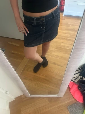 Mörkblå jeanskjol med fickor - Säljer en mörkblå jeanskjol i klassisk modell med synliga sömmar och fickor fram. Kjolen har en kort längd och stängs med knapp och dragkedja. Perfekt att matcha med en enkel topp eller hoodie.