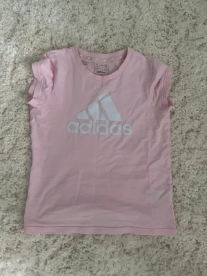 rosa t-shirt - Snygg ljusrosa t-shirt från Adidas med klassisk vit logga framtill. T-shirten har korta ärmar och rund halsringning. Tillverkad i mjuk bomull som känns skön mot huden. Perfekt för en sportig och avslappnad stil.🥰pris kan diskuteras