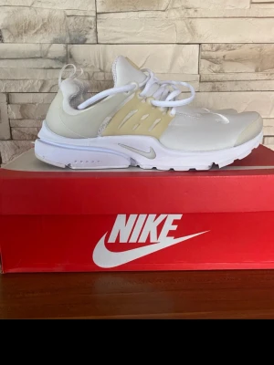 Nike vita och beige sneakers - Snygga Nike sneakers i vitt och beige med mesh- och syntetmaterial. Skorna har en låg profil, klassisk snörning och en bekväm, vadderad plös. Perfekta för dig som gillar stilrena och sportiga sneakers med modern design.