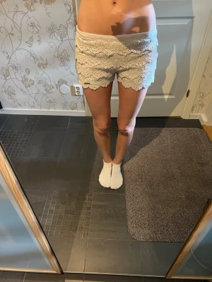 Vita spetsdetaljerade shorts - Säljer ett par vita shorts med flera lager av spets och volangdetaljer. De har en låg midja och är perfekta för sommarens alla tillfällen. Materialet känns lätt och luftigt, vilket gör dem riktigt sköna att bära. Dom är i storlek w28 så skulle säga som en S. Typ helt nytt skick. Dom är lite off White/ grädd vit i färgen.