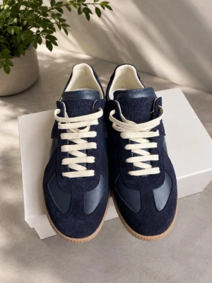 Mörkblå Maison Margiela gats - Snygga mörkblå sneakers från Maison Margiela med ovandel i mocka och läder, vita snören och klassisk gummisula. Skorna har en låg silhuett och stilren design som passar till det mesta. Perfekta för dig som gillar minimalistisk och trendig stil.