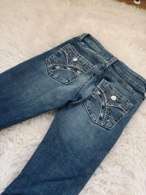 y2k jeans! - Säljer ett par blå jeans med snygga broderade detaljer på bakfickorna och silvriga knappar. Jeansen har en klassisk femficksmodell och en något tvättad look. Perfekta för dig som vill ha något extra på fickorna!