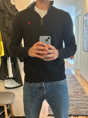 Svart halvzip från Polo Ralph Lauren - Klassisk svart stickad tröja från Polo Ralph Lauren med halv dragkedja och röd broderad logga på bröstet. 