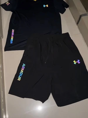 Svarta shorts från Under Armour - Snygga svarta shorts från Under Armour med regnbågsfärgad logga och text på benet. Shortsen har snörning i midjan och är perfekta för träning eller chill. Tillverkade i ett mjukt och lätt material som andas.