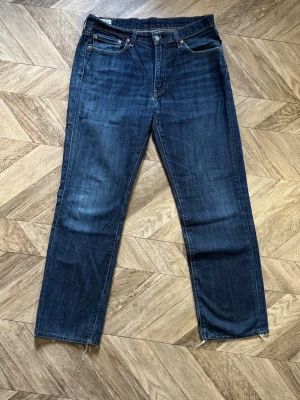 Mörkblåa Levi's 514 - Säljer ett par mörkblå jeans med rak passform och klassisk femficksdesign. Jeansen har råa, avklippta benslut och kontrastsömmar. Materialet är denim i bomull och de har en tidlös look som passar till det mesta.