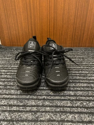 Nike Air Vapormax Plus svarta sneakers - Snygga svarta Nike Air Vapormax Plus sneakers med tydlig logga på plösen. Skorna har en chunky sula, svarta skosnören och detaljer i vitt. Ovandelen är i textil och syntetmaterial med en modern, sportig look. Använd max 5 gånger. Som helt nya, jättefräscha. 