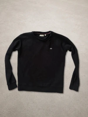 Svart sweatshirt från GANT - Svart sweatshirt från GANT med rund halsringning och diskret logga på bröstet. Tröjan har ribbade muddar vid ärmslut och nederkant. 