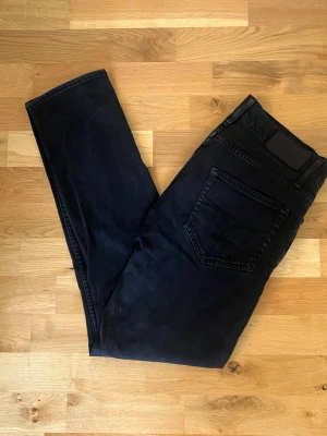 Svarta slim fit jeans - Säljer ett par svarta slim fit jeans med klassisk femficksdesign och knappgylf. Jeansen har raka ben och är tillverkade i ett mjukt denimtyg som ger en skön passform. Perfekta för dig som gillar en stilren och enkel look.