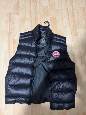 Svart dunväst från Canada Goose - Snygg svart dunväst från Canada Goose med klassisk logopatch på bröstet. Västen är helt ny och äkta ingen kopia 