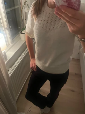 Vit stickad topp med kort ärm - Säljer en söt vit stickad topp från Holly & Whyte med korta ärmar och ribbade muddar. Tröjan har ett fint hålmönster upptill och rund halsringning. 