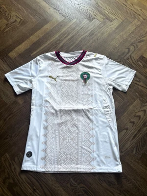 Marocko Borta 26/27 Fotbollströja  - Marocko borta 26/27 Fotbollströja i storlek S. tröjan är i perfekt skick och har aldrig använts förut. Suverän kvalité och perfekt för fotbolls älskare. 