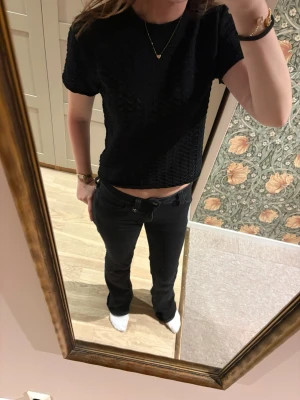 Svart kortärmad spetsstickad topp - Säljer en svart, kortärmad topp med spetsstickat mönster och lätt transparent känsla. Toppen är croppad och har en rund halsringning. Perfekt för dig som gillar en enkel men ändå detaljrik stil.