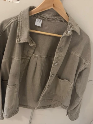 Grön  jeansjacka - Snygg  grön jeansjacka i  modell med stora framfickor och tryckknappar. Klassisk krage och avslappnad passform, perfekt för en cool och avslappnad stil. Jackan har synliga sömmar och är tillverkad i kraftigt jeanstyg.