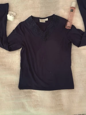 Mörkblå långärmad topp med spets - Snygg mörkblå långärmad topp med v-ringning och dekorativ spetsdetalj längs halsringningen. Perfekt att styla med jeans eller kjol för en trendig look. Materialet känns mjukt och följsamt mot huden.🫰🏻💓